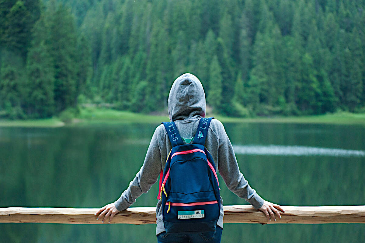 Person steht alleine vor einem See mit Hoody und Rucksack zum Thema New Work und introvertierte Personen Person steht alleine vor einem See mit Hoody und Rucksack zum Thema New Work und introvertierte Personen