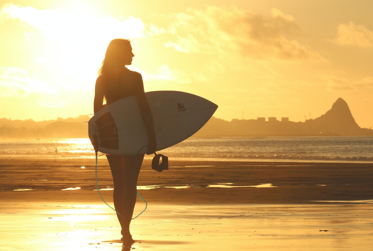 Surfer Girl am Stand mit Sonnenuntergang im Hintergrund Surfer Girl am Stand mit Sonnenuntergang im Hintergrund