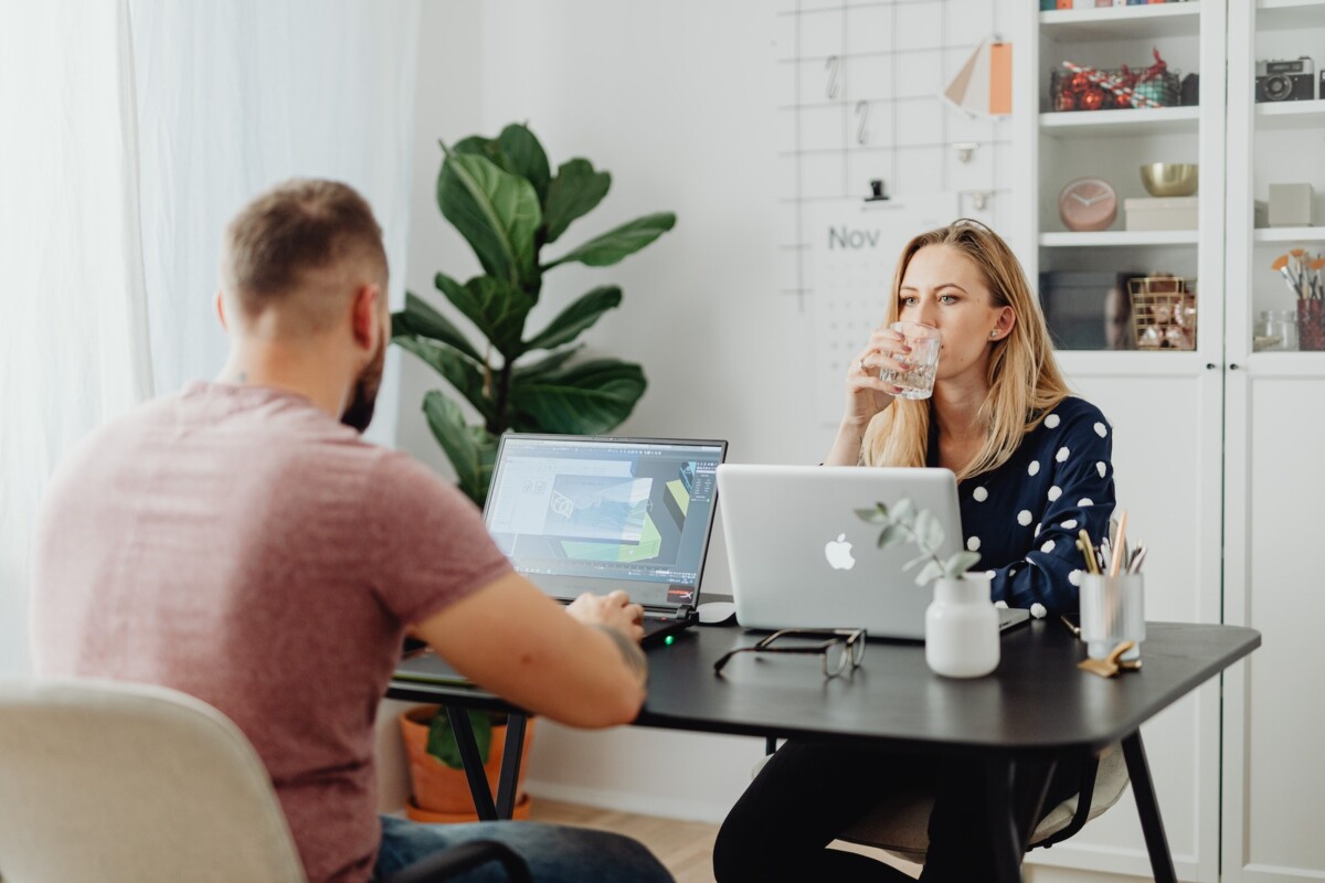 New Work im Home Office sitzt sich im Wohnzimmer an einem Tisch ein Pärchen gegenüber