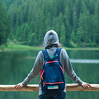 Person steht alleine vor einem See mit Hoody und Rucksack zum Thema New Work und introvertierte Personen